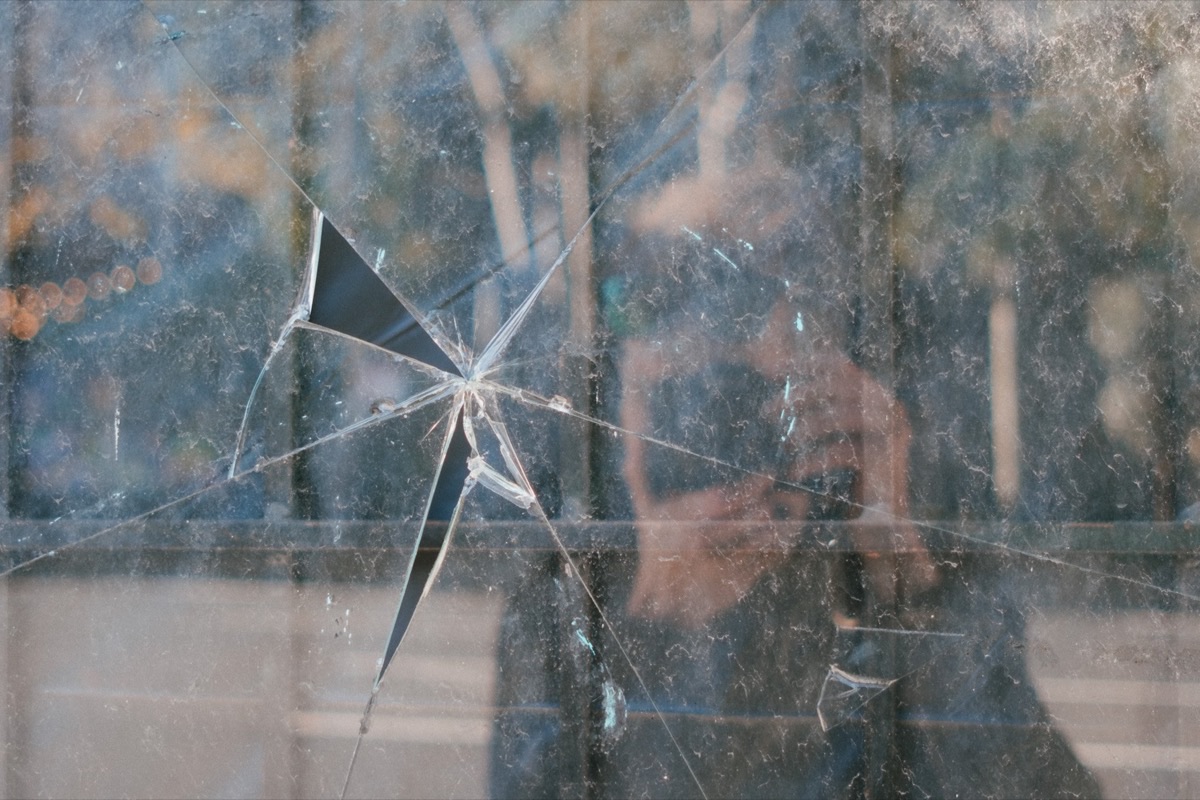 Self-portrait ghosted in shattered glass, camera raised